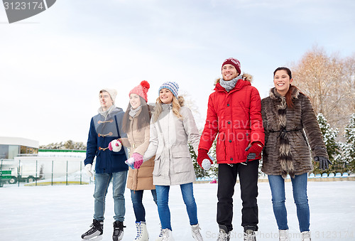 Image of happy friends ice skating on rink outdoors