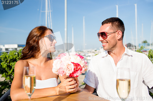 Image of smiling couple with bunch and champagne at cafe