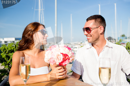 Image of smiling couple with bunch and champagne at cafe