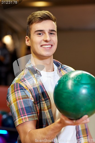 Image of happy young man holding ball in bowling club