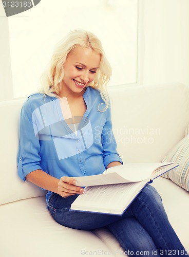 Image of smiling woman reading book and sitting on couch