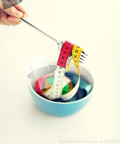 Image of woman hand with fork, bowl and measuring tape