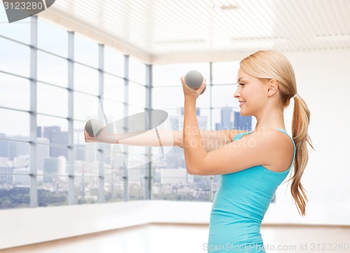 Image of smiling woman with dumbbells flexing biceps in gym