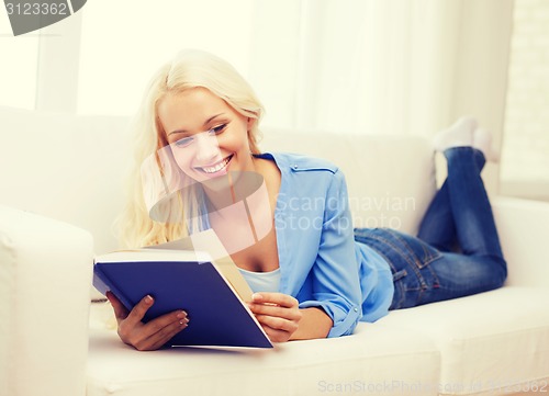 Image of smiling woman reading book and lying on couch