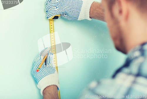 Image of closeup of male in gloves measuring wall with tape