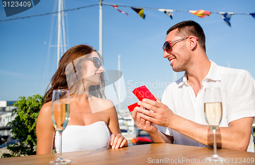 Image of smiling couple with champagne and gift at cafe