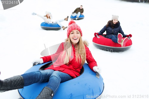 Image of group of happy friends sliding down on snow tubes