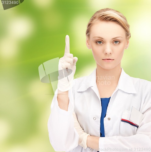 Image of smiling young female doctor pointing her finger up