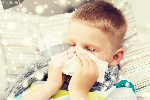 Image of ill boy blowing nose with tissue at home