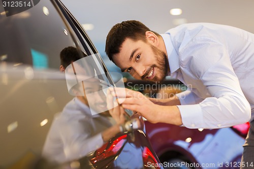 Image of happy man touching car in auto show or salon