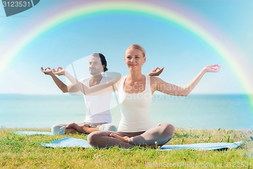 Image of smiling couple making yoga exercises outdoors