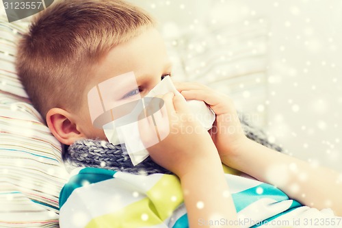 Image of ill boy blowing nose with tissue at home