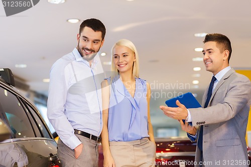 Image of happy couple with car dealer in auto show or salon