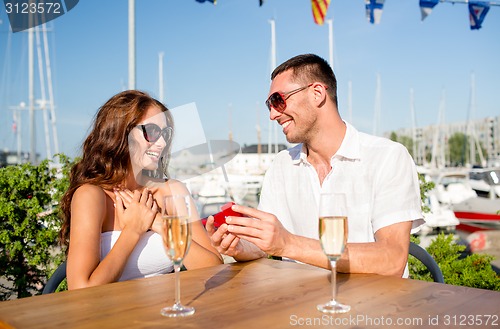 Image of smiling couple with champagne and gift at cafe