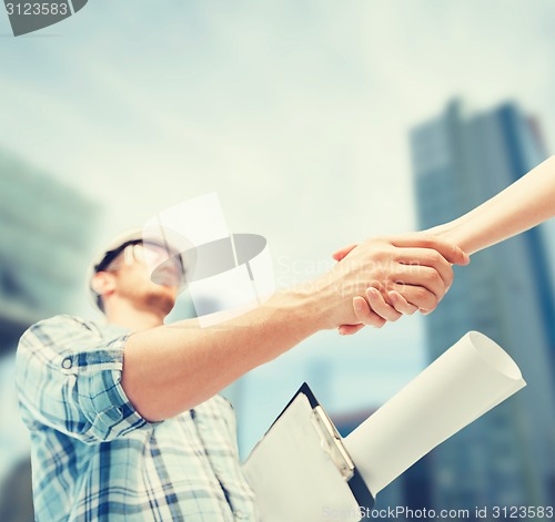 Image of builder with blueprint shaking partner hand