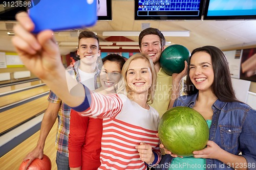 Image of happy friends with smartphone in bowling club