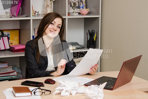 Image of Business girl holding paper looks into the frame and smiling