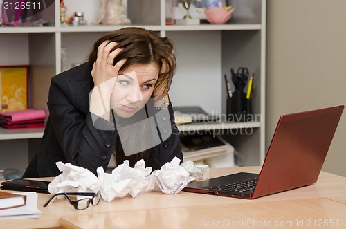 Image of The girl at computer with a bunch of crumpled sheets paper