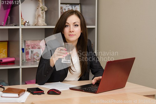 Image of Business woman at the computer holding a glass of water