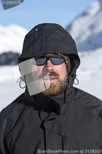 Image of Young man in snowy mountain landscape looks into the camera