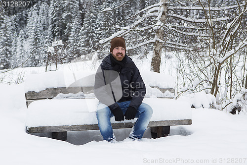 Image of Young man is sitting on a snowy park bench