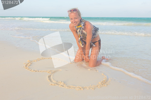 Image of Woman drawing heart on the sand.