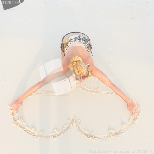 Image of Woman drawing heart on the sand.