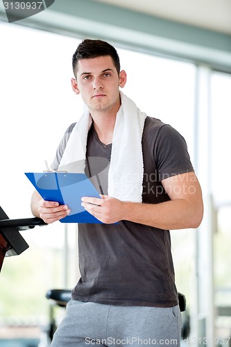 Image of trainer with clipboard standing in a bright gym