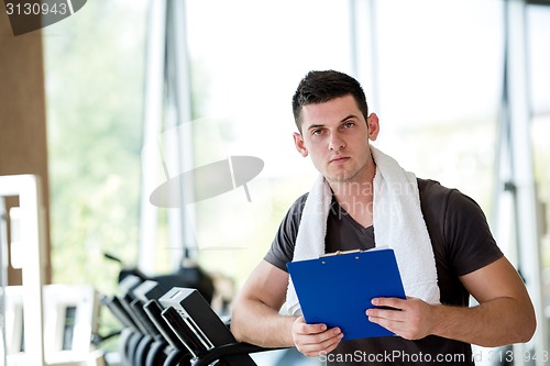 Image of trainer with clipboard standing in a bright gym