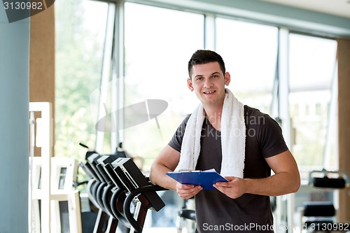 Image of trainer with clipboard standing in a bright gym