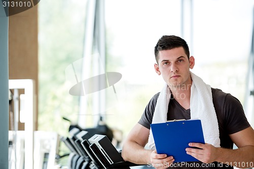 Image of trainer with clipboard standing in a bright gym