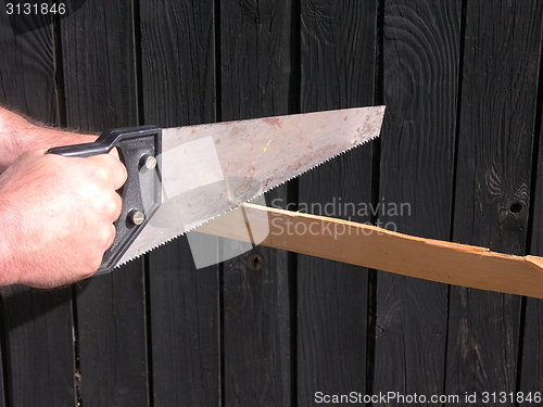 Image of Cutout with hand and hand saw in front of a wooden wall