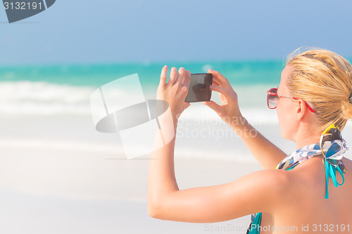 Image of Woman taking photo on the beach.