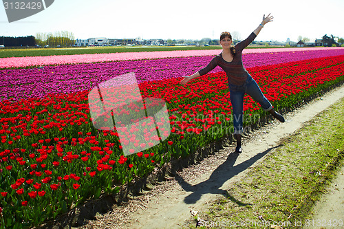 Image of beautiful young woman having fun on the meadow with red and yellow  flowers tulips, outdoors