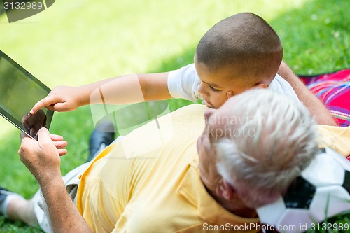 Image of grandfather and child in park using tablet