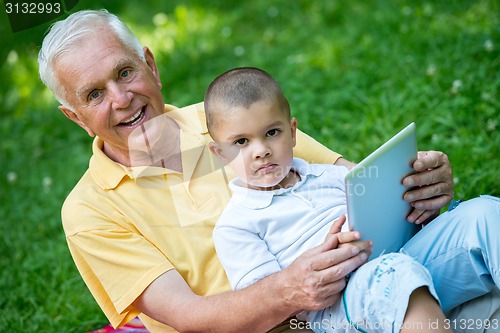 Image of grandfather and child in park using tablet