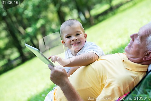 Image of grandfather and child in park using tablet