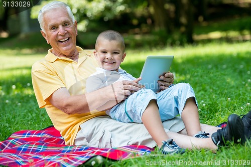 Image of grandfather and child in park using tablet