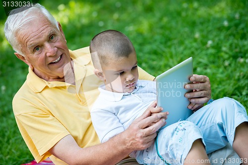Image of grandfather and child in park using tablet
