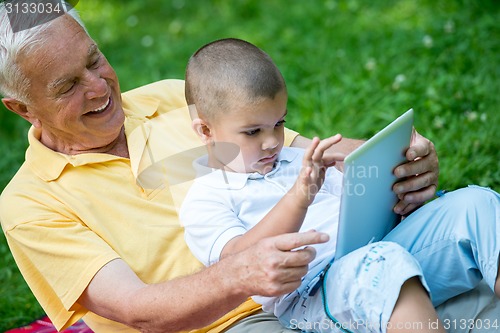 Image of grandfather and child in park using tablet