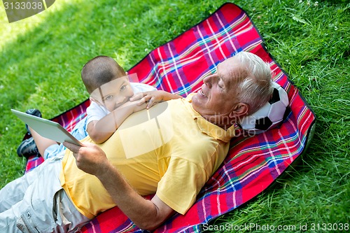 Image of grandfather and child in park using tablet