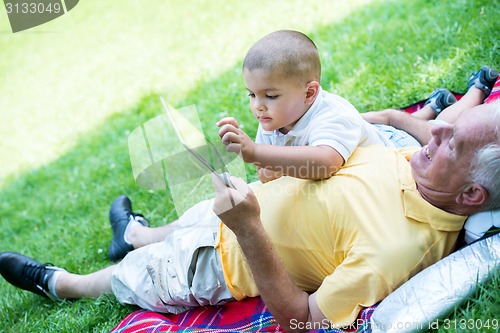 Image of grandfather and child in park using tablet