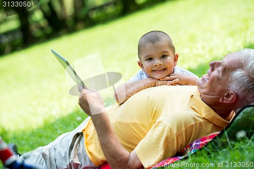 Image of grandfather and child in park using tablet