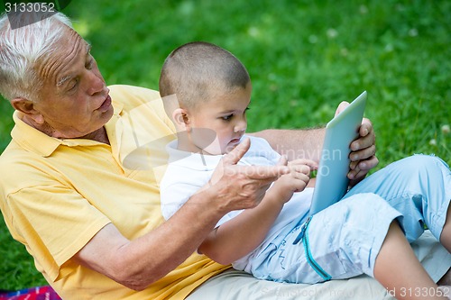 Image of grandfather and child in park using tablet