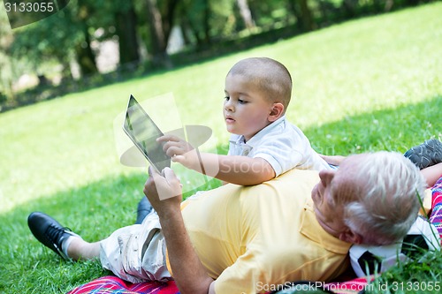 Image of grandfather and child in park using tablet