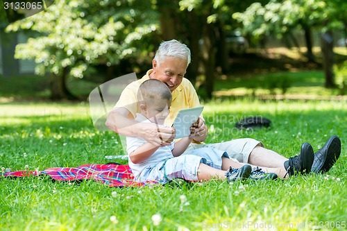 Image of grandfather and child in park using tablet