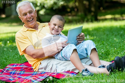 Image of grandfather and child in park using tablet