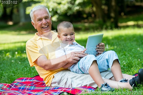 Image of grandfather and child in park using tablet
