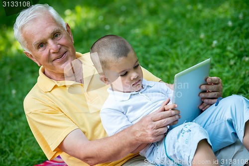 Image of grandfather and child in park using tablet