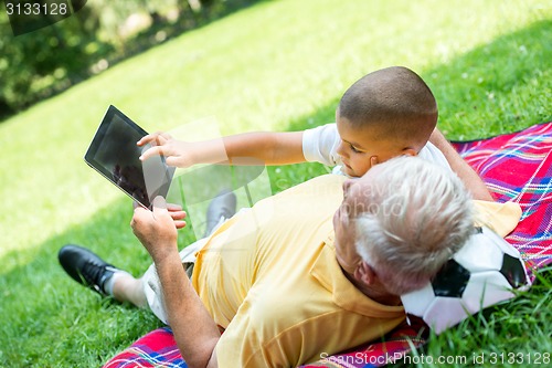 Image of grandfather and child in park using tablet